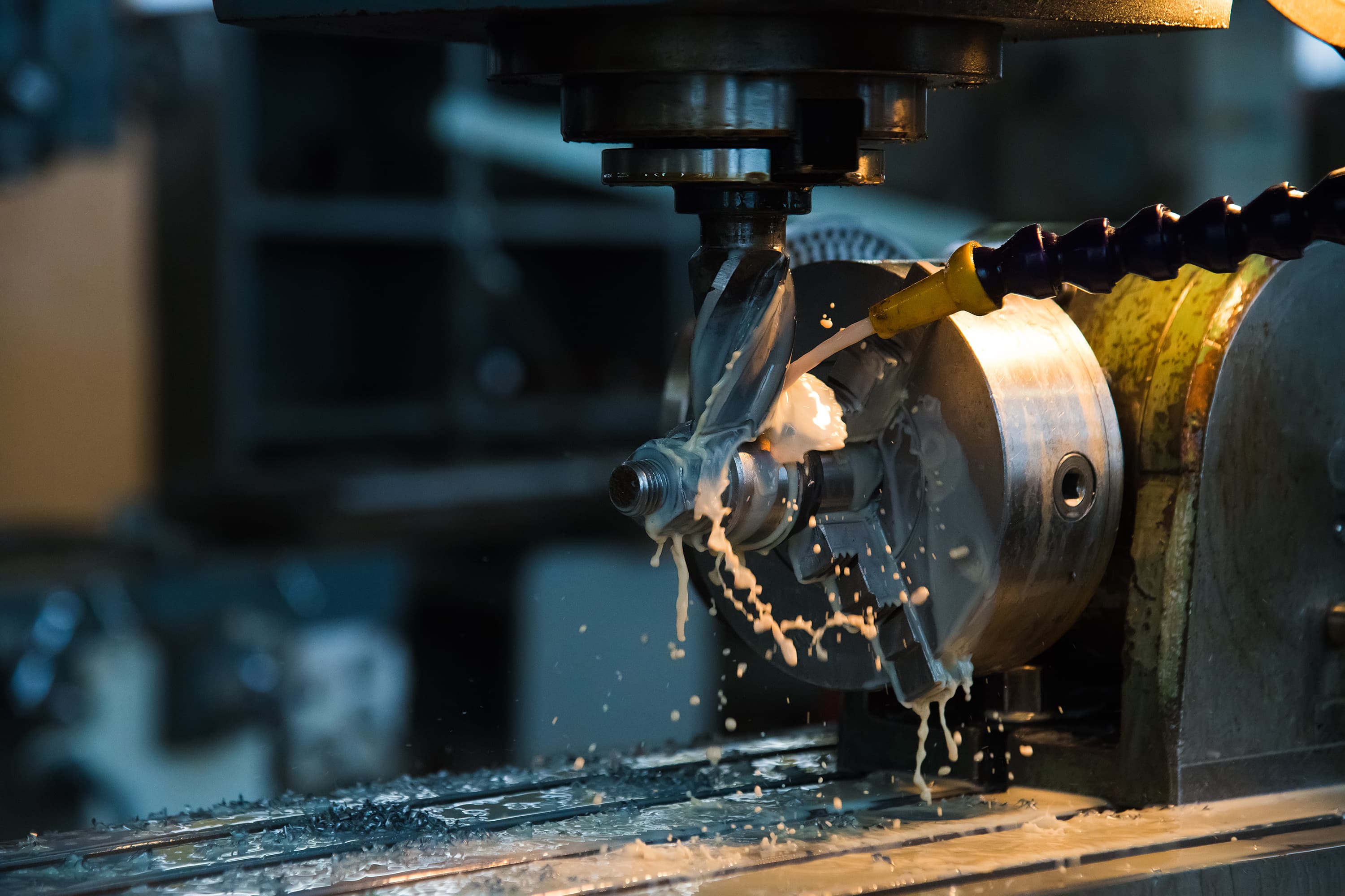 An end mill cutting a steel component under flood coolant, chips collecting in the machine bed