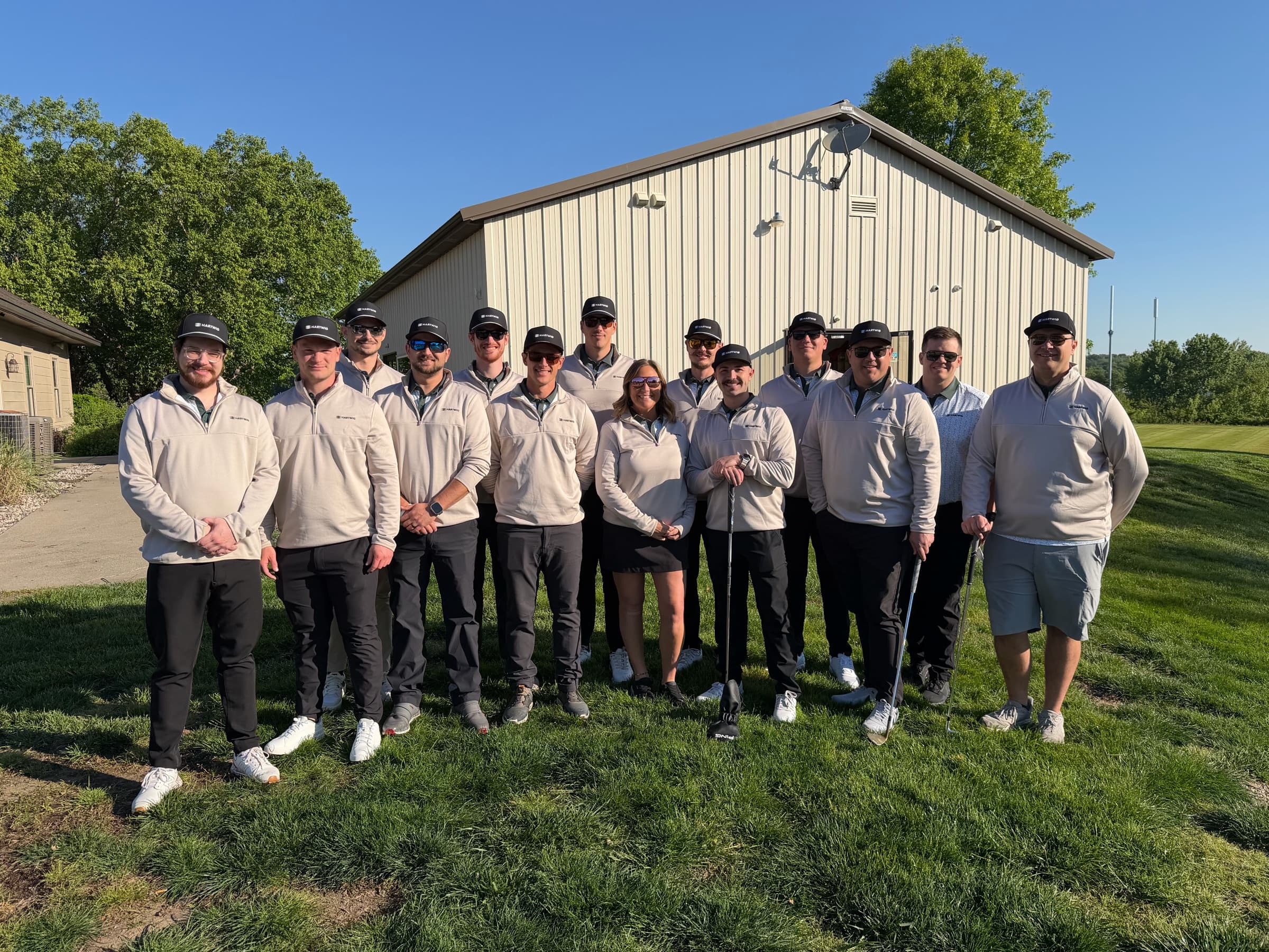 A team of fifteen in matching quarter-zips and caps posing on the grass at the chapter golf outing